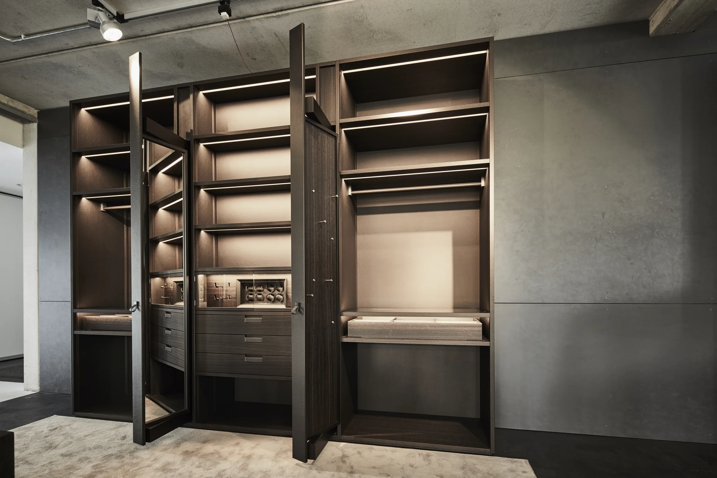 Begehbare Ankleide in dunklem Holz mit beleuchteter Taschenvitrine und Spiegelfläche