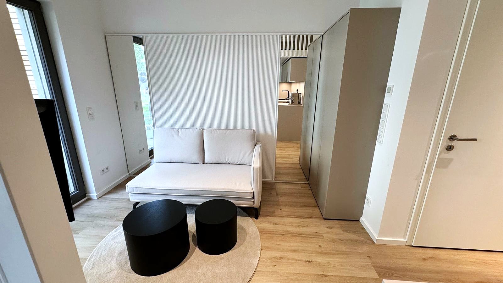 Ein-Raum-Apartment Berlin von HOME Schlafen & Wohnen: Wohnbereich mit Sofa und Hockern